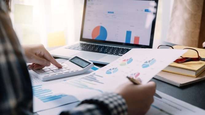 Person analyzing financial charts with calculator and laptop